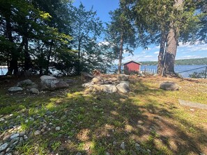 En vacker och naturlig utomhusmiljö med en röd stuga, stora stenar och träd nära ett vattendrag.