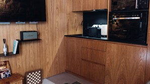 Een compacte keuken met houten kastjes, een zwart aanrecht, een magnetron en een aan de muur bevestigde televisie.