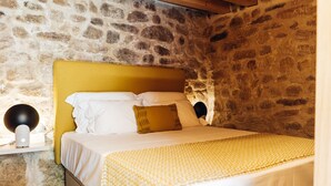 Een bed in een kamer met stenen muren, een geel hoofdeinde, wit beddengoed en een gele deken.