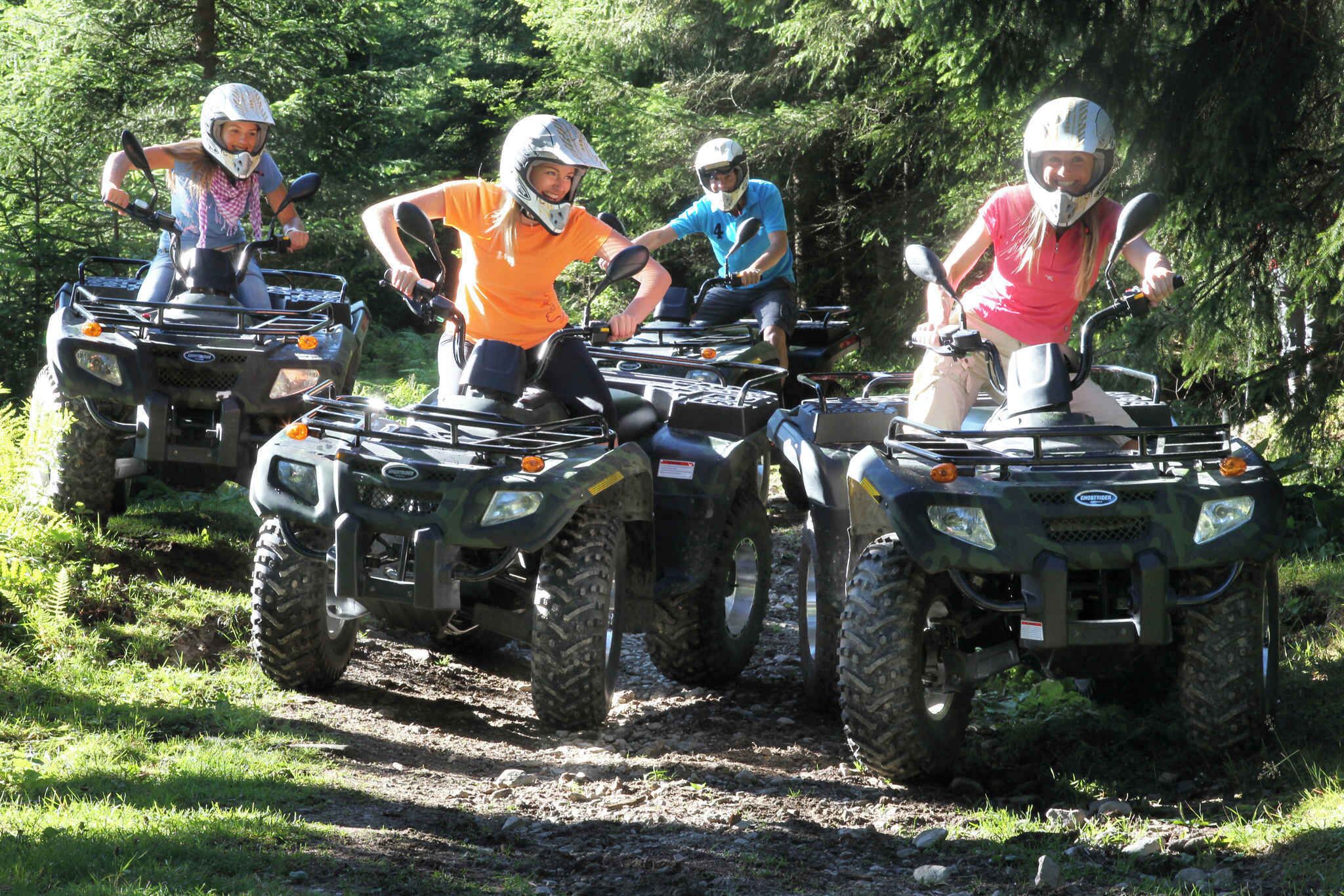 Four people on ATVs on a dirt path surrounded by greenery.