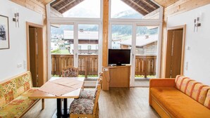Una habitación acogedora con techo de madera, un ventanal grande, televisión, sofá y una mesa de comedor con sillas.