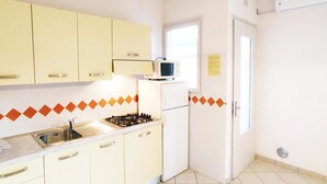 Eine kompakte Küche mit gelben Schränken, einem weißen Kühlschrank, einer Mikrowelle und einem Gasherd.