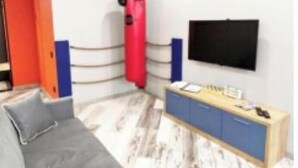 Una camera da letto moderna con un divano grigio, un comò in legno, un sacco da boxe rosso e una televisione a schermo piatto montata a parete.