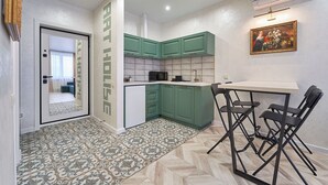 A compact kitchen with green cabinets, a microwave, and a dining area with a table and chairs.