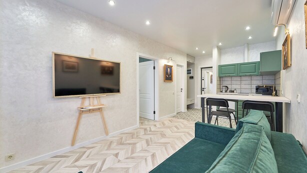 A modern living room with a flat-screen TV mounted on the wall, a wooden easel, and a green sofa.