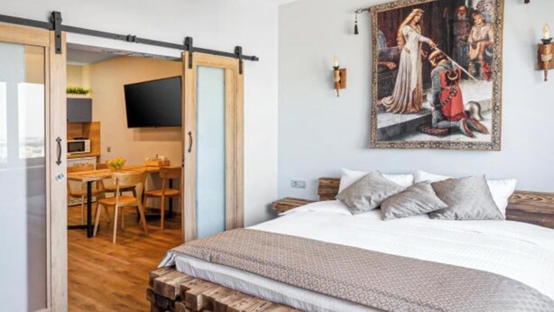 Slaapkamer met een groot bed, een houten hoofdbord, een schilderij aan de muur en een schuifdeur naar een keukenhoek.