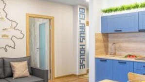 Een moderne woonkamer met een grijze bank, een houten eettafel en een keuken met blauwe kastjes.