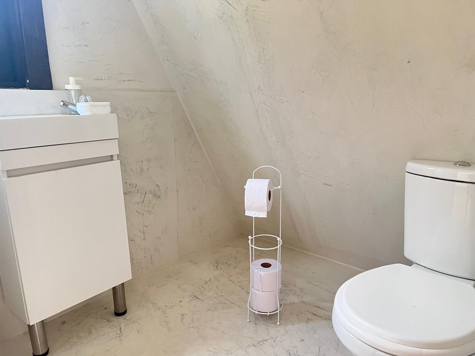 Baño pequeño y blanco con inodoro, lavamanos y dispensador de papel higiénico.