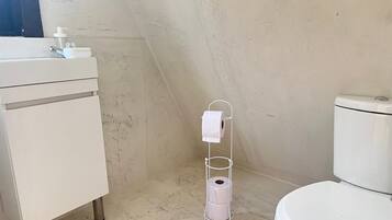 Baño pequeño y blanco con inodoro, lavamanos y dispensador de papel higiénico.