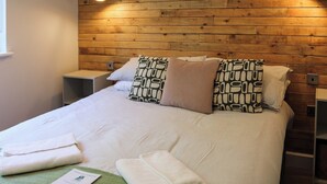 Un lit bien fait, agrémenté d’oreillers à motifs, une table de chevet et un panneau mural en bois.