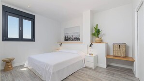 A bedroom with a bed, bedside tables, a nightstand, a wall-mounted lamp, a framed picture, a potted plant, and a wicker basket. - Solaga - Chinchilla (Málaga)