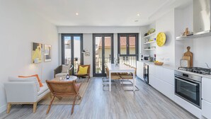 A modern kitchen with white cabinets, a dining area with a white table and chairs, and a large window overlooking a balcony. - Solaga - Chinchilla (Málaga)