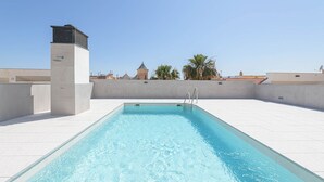 A rooftop swimming pool with clear blue water, surrounded by white tiled flooring and a concrete wall. - Solaga - Chinchilla (Málaga)