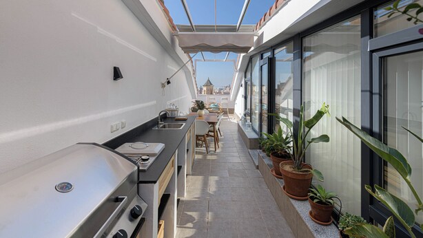 A narrow balcony with a grill, potted plants, and a dining area with chairs and a table. - Solaga - Chinchilla (Málaga)