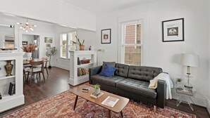 Ein geräumiges Wohnzimmer mit einem dunkelbraunen Ledersofa, einem Couchtisch und einem Essbereich mit weißem Tisch und Stühlen.