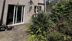 Een twee verdiepingen tellend huis met een grote schuifdeur, een schotelantenne en een tuin met diverse planten.