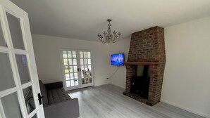 Een woonkamer met een grijze bank, een open haard, een aan de muur bevestigde televisie en een kroonluchter.