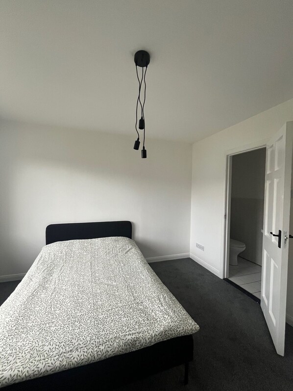 Ett sovrum med en säng, en dörr som leder till ett badrum och en hängande lampa.