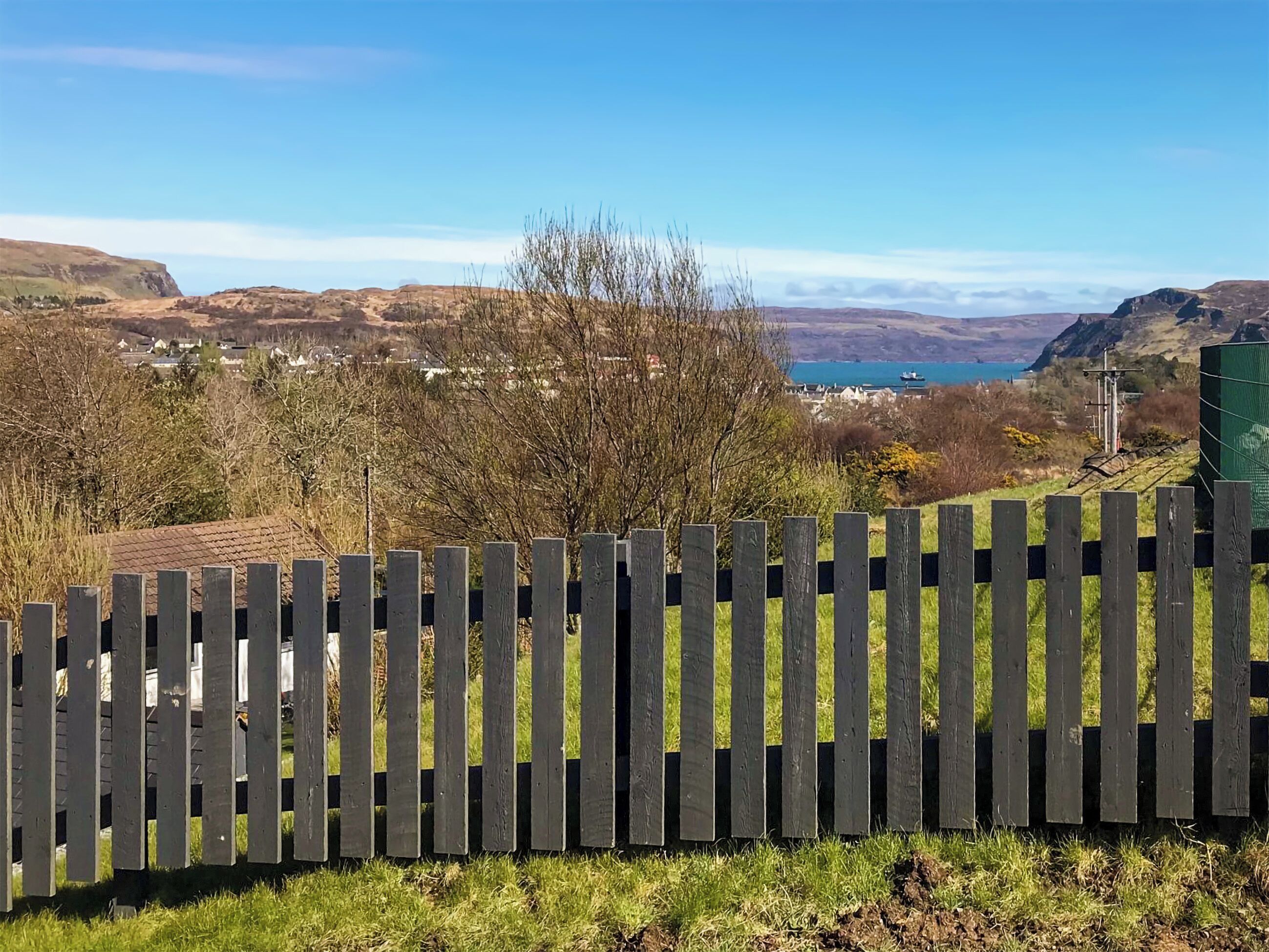 Una recinzione in legno in un ambiente rurale con vista su un lago e colline lontane.