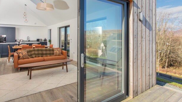 Un interior moderno con un ventanal corredero que da a una terraza, un sofá y una zona de cocina.