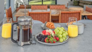 Desayuno con una cafetera, croissant, fruta y vasos de jugo sobre una mesa.