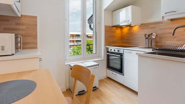 Una cocina moderna con armarios blancos, horno empotrado y ventana con vistas a un balcón.