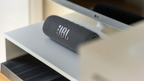 Un altavoz JBL sobre un soporte blanco, junto a un monitor de computadora.