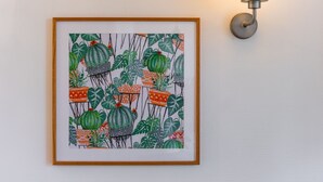 Un cuadro enmarcado con cactus y hojas en una pared, junto a una lámpara fijada a la pared.
