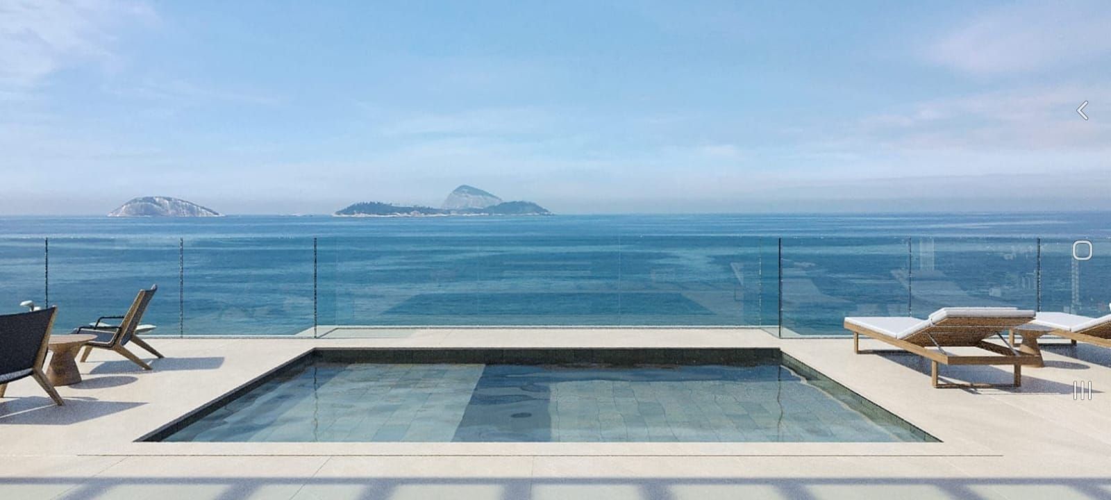 A rooftop infinity pool with lounge chairs and a clear view of the ocean and islands.
