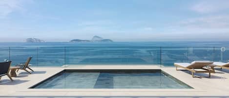 Una piscina infinita en la azotea con sillones de descanso y vistas despejadas al océano y a las islas.