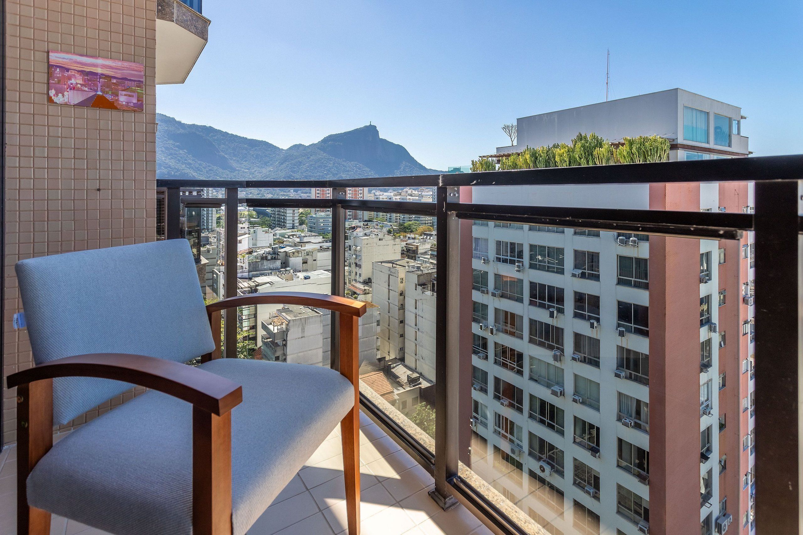 A balcony with a chair, a tiled wall, and a view of a cityscape with buildings and mountains.