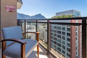 A balcony with a chair, a tiled wall, and a view of a cityscape with buildings and mountains. - (1402) 2 Suítes, Vista para o Mar e Cristo (Rio de Janeiro)