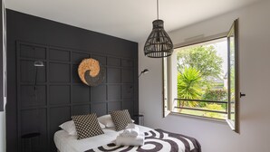 A bedroom with a bed, a large window, a hanging light fixture, and a wall-mounted decorative item. - Comtesse Lili - Maison proche de la mer, jardin (La Richardais)