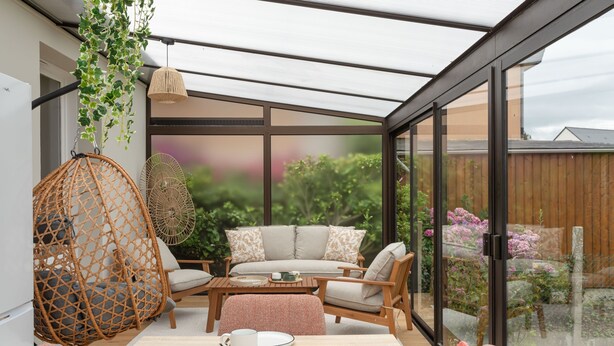 A sunlit room with a glass enclosure, wicker hanging chairs, a sofa, and a dining table with croissants and a mug. - Comtesse Lili - Maison proche de la mer, jardin (La Richardais)