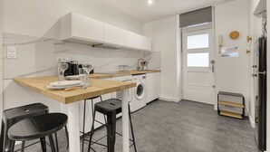 A modern kitchen with white cabinets, a wooden countertop, a washing machine, and a sink.