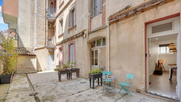 A courtyard with a table and chairs, potted plants, and a building entrance.