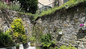 A courtyard with potted plants, a stone wall, and a white door. - 3 bedroom accommodation in Coldstream, near Kelso (Coldstream, near Kelso)