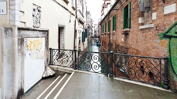 A narrow alleyway with a metal railing, brick buildings, and a wet pavement. - San Polo Apartment by Ca-sa Check (Venice)