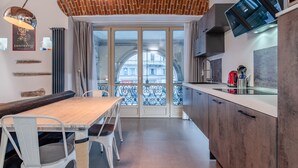 A modern kitchen with a wooden dining table, white chairs, and a large window with a view of a building. - Suite Queen Apartments (Turin)