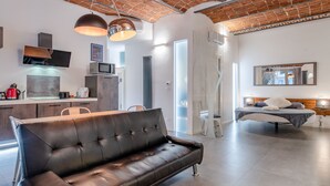 A modern living space with a leather sofa, a dining area, a kitchen, and a bedroom with a large bed and a mirror. - Suite Queen Apartments (Turin)