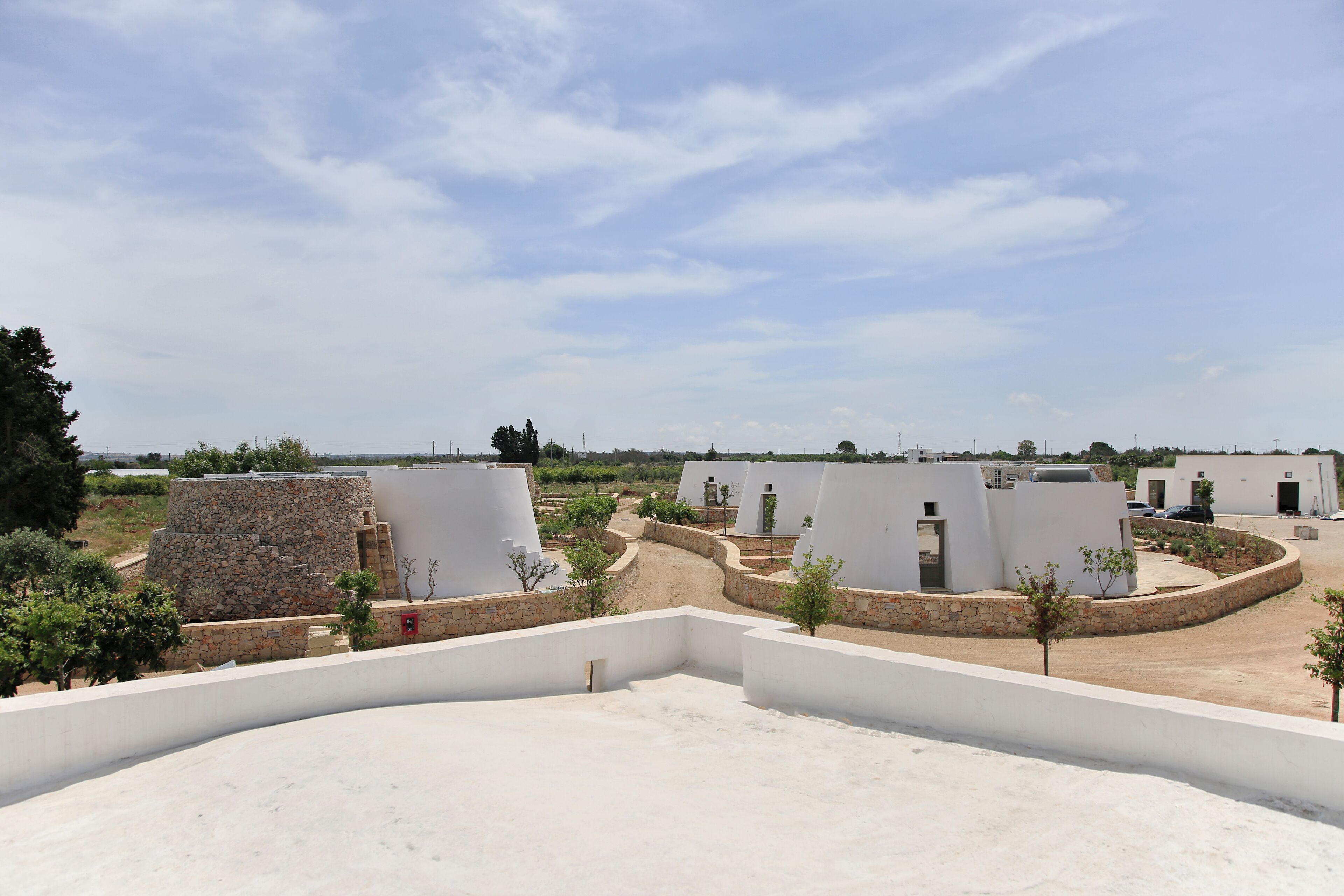 A residential area with modern white buildings, stone walls, and a clear sky.