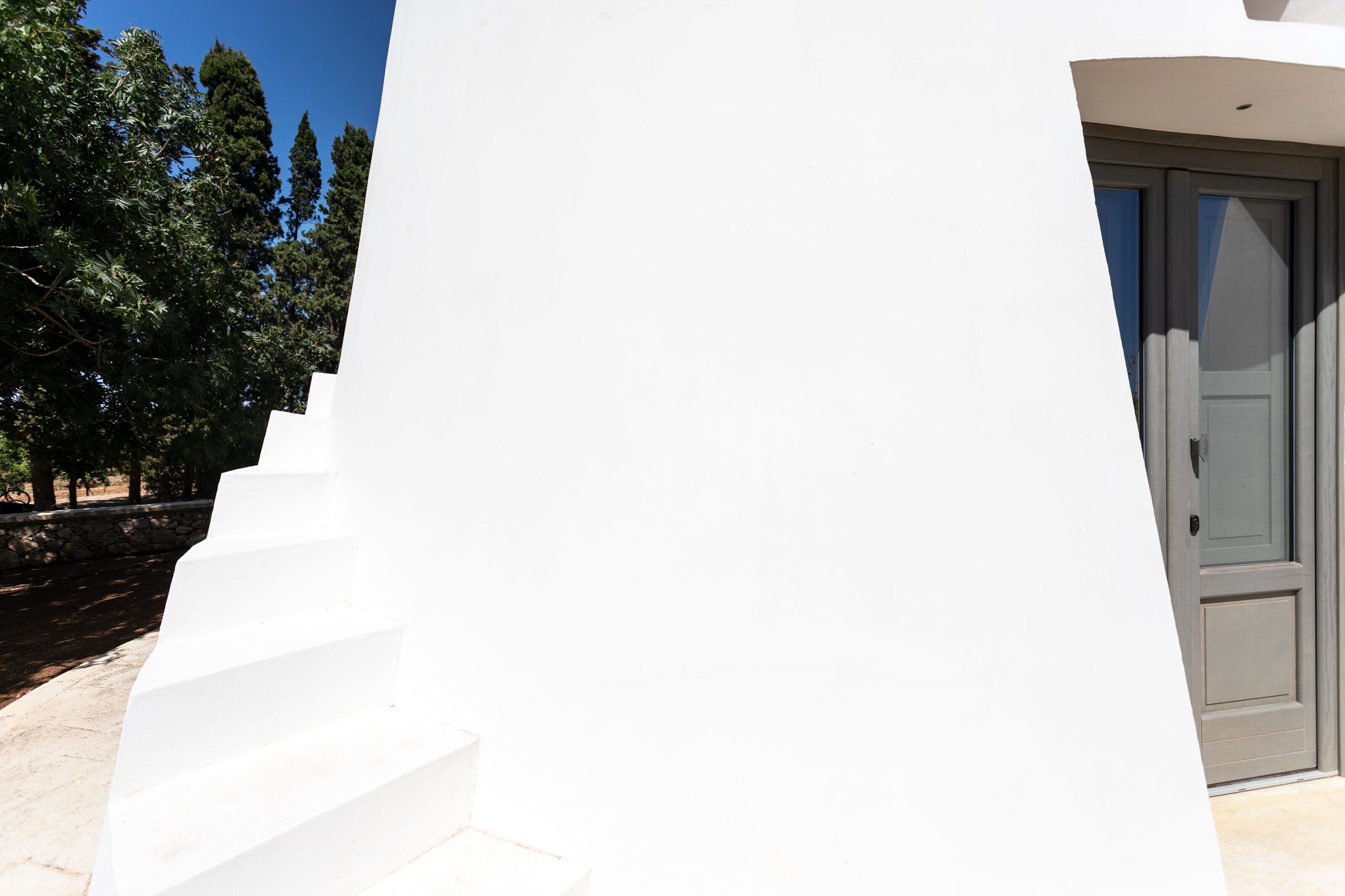 Un bâtiment blanc avec une porte grise et un escalier menant à l’entrée.
