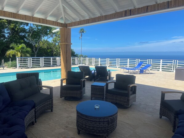 A covered outdoor area with wicker furniture, a pool, and a view of the ocean.