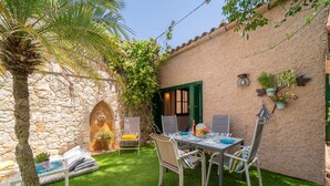 A patio with a stone wall, a palm tree, and a table with chairs. - Ca na Sabatera Semi-detached House with Private Pool in Ariany (Ariany)