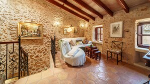 A rustic room with exposed stone walls, a wooden ceiling, and a tiled floor. There is a sofa, a chair, and a small table with a lamp. - Ca na Sabatera Semi-detached House with Private Pool in Ariany (Ariany)