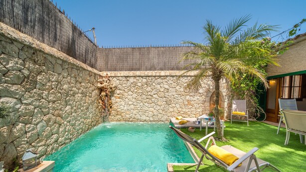 A swimming pool with stone walls, a palm tree, and outdoor furniture. - Ca na Sabatera Semi-detached House with Private Pool in Ariany (Ariany)