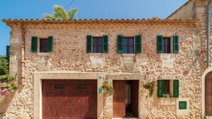 A stone building with a large wooden door, multiple windows with green shutters, and a small balcony with flowers. - Ca na Sabatera Semi-detached House with Private Pool in Ariany (Ariany)