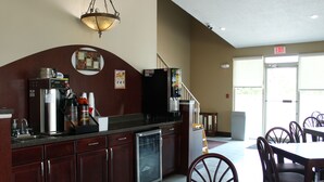 A kitchen with a coffee machine, refrigerator, and a sink. There are chairs and a table in the dining area. - Boarders Inn & Suites (Lamar)