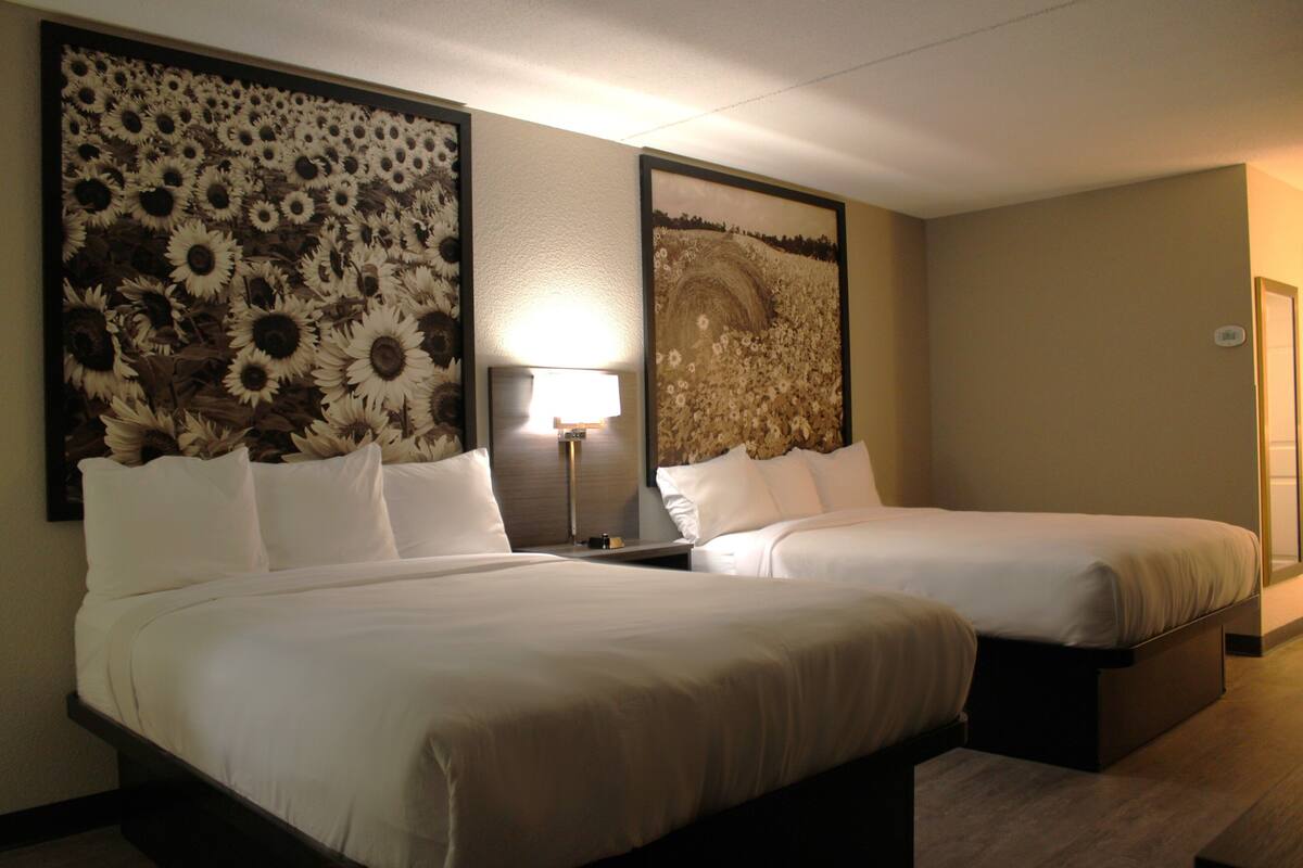 A hotel room with two beds, a large floral artwork on the wall, a bedside lamp, and a door to the right.