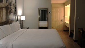 A hotel room with a large bed, a bedside lamp, a door, and a wall-mounted mirror. - Boarders Inn & Suites (Lamar)